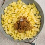 Chopped apples in a skillet topped with brown sugar and spices, ready to be cooked.