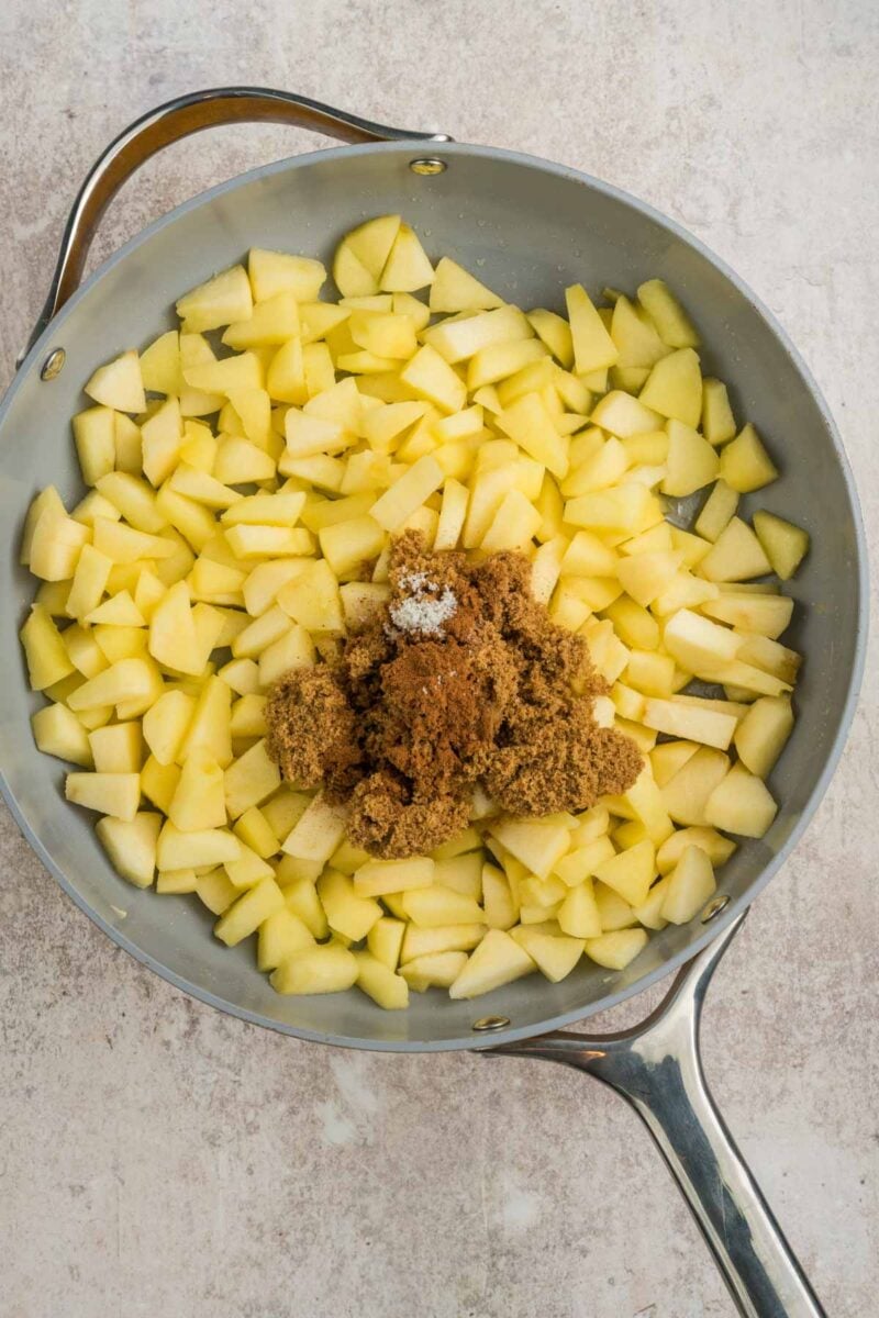 Chopped apples in a skillet topped with brown sugar and spices, ready to be cooked.