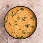 A skillet filled with creamy risotto mixed with spinach and herbs sits on a light-colored tiled surface.