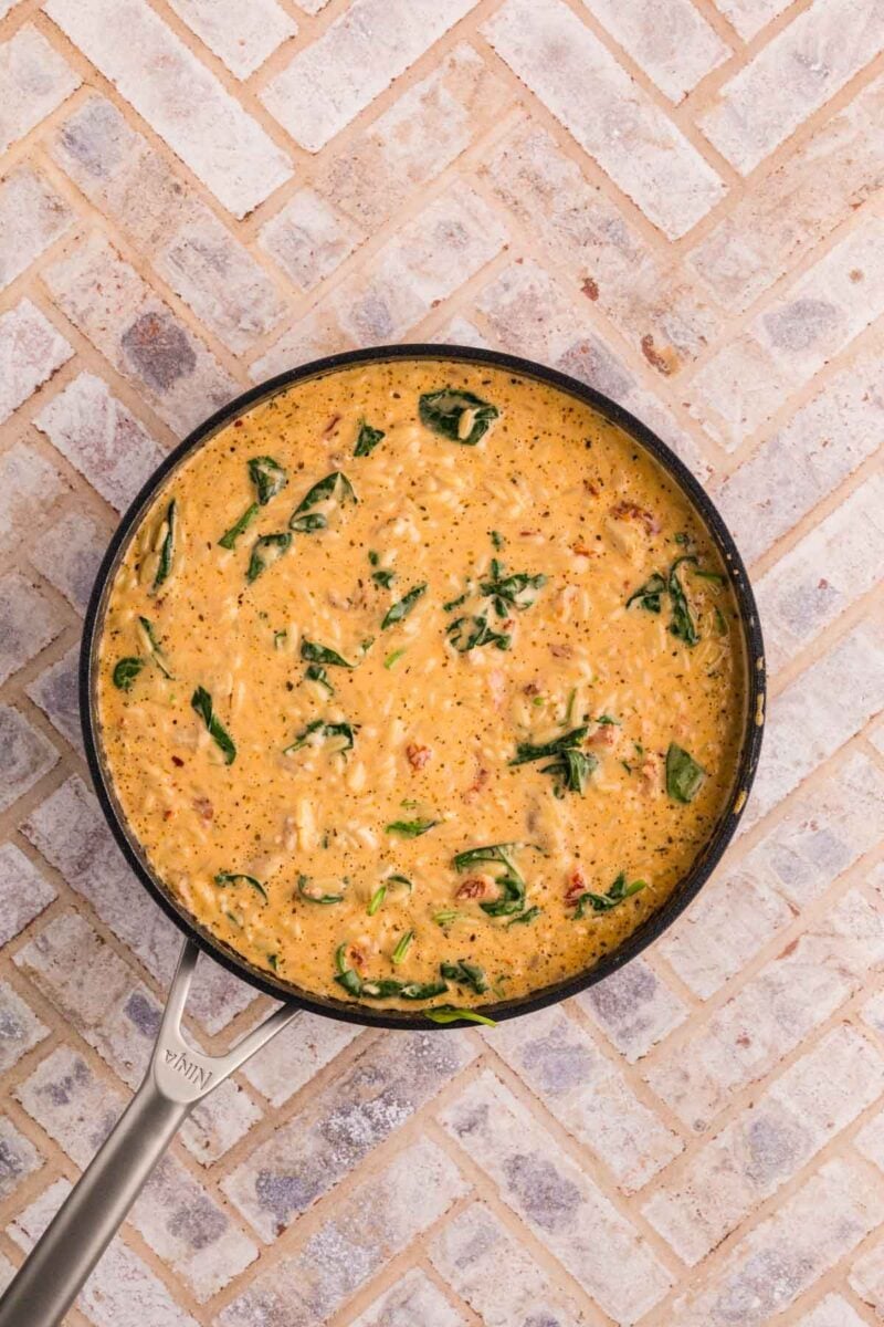 A skillet filled with creamy risotto mixed with spinach and herbs sits on a light-colored tiled surface.