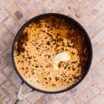 A skillet with a creamy sauce and browned bits, topped with a dollop of butter, sits on a light tile surface.