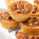 Close-up of pecan tarts stacked on a marble surface, with whole pecans in front. Text reads āPecan Tarts Easy!ā and āsouthernfoodandfun.comā at the bottom.
