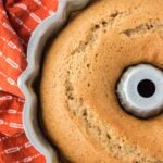 A golden-brown bundt cake in a metal pan next to an orange patterned cloth.