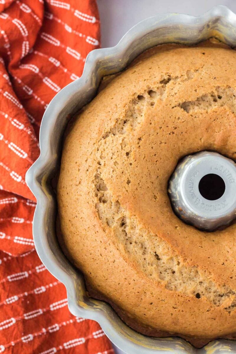 A golden-brown bundt cake in a metal pan next to an orange patterned cloth.