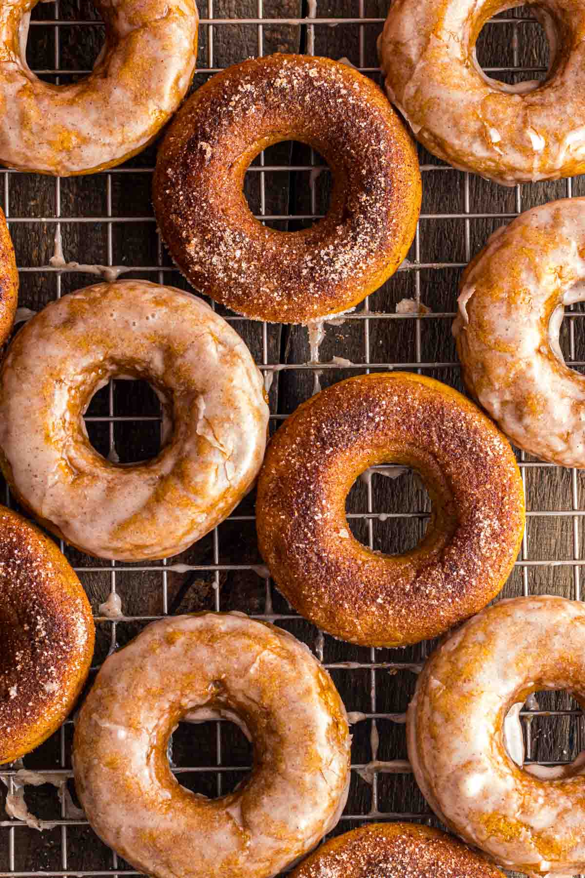 Glazed and cinnamon sugar pumpkin donuts are arranged on a cooling rack.