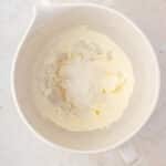 A white mixing bowl containing creamed butter and sugar on a light countertop, viewed from above.