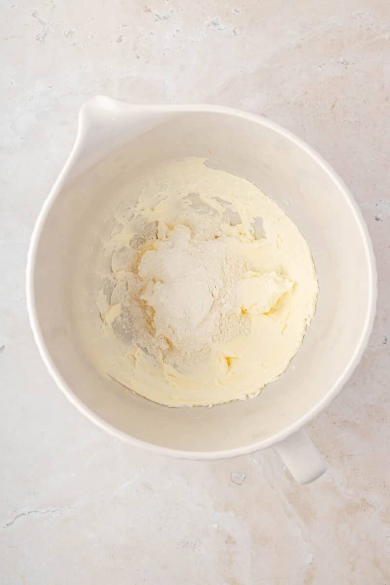 A white mixing bowl containing creamed butter and sugar on a light countertop, viewed from above.