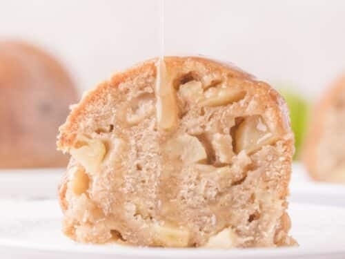 A slice of apple cake on a white plate with glaze being drizzled on top.