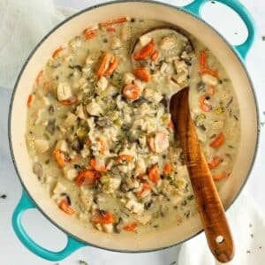 Creamy chicken and wild rice soup with sliced carrots in a teal enameled Dutch oven with a wooden spoon.