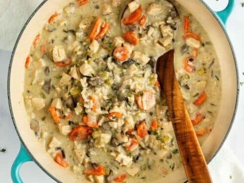 Creamy chicken and wild rice soup with sliced carrots in a teal enameled Dutch oven with a wooden spoon.
