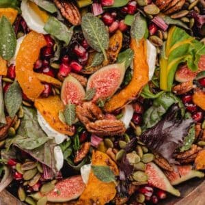 Salad featuring roasted squash, halved fresh figs, pomegranate seeds, pecans, pumpkin seeds, and dollops of soft cheese.