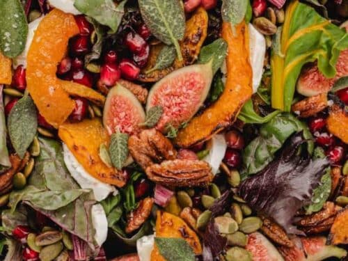 Salad featuring roasted squash, halved fresh figs, pomegranate seeds, pecans, pumpkin seeds, and dollops of soft cheese.