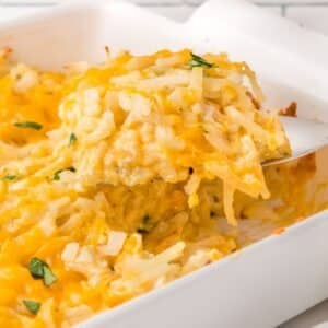 A spatula lifting a serving of cheesy potato casserole from a white baking dish.