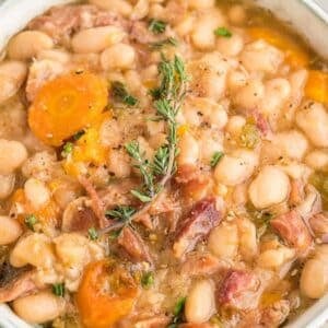 A bowl of white bean and ham soup garnished with fresh thyme.