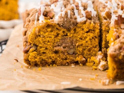 A slice of pumpkin coffee cake topped with streusel, pecans, and a white glaze.
