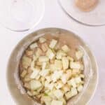 Chopped apples in a mixing bowl with cake batter, with a second bowl and a spoon nearby.