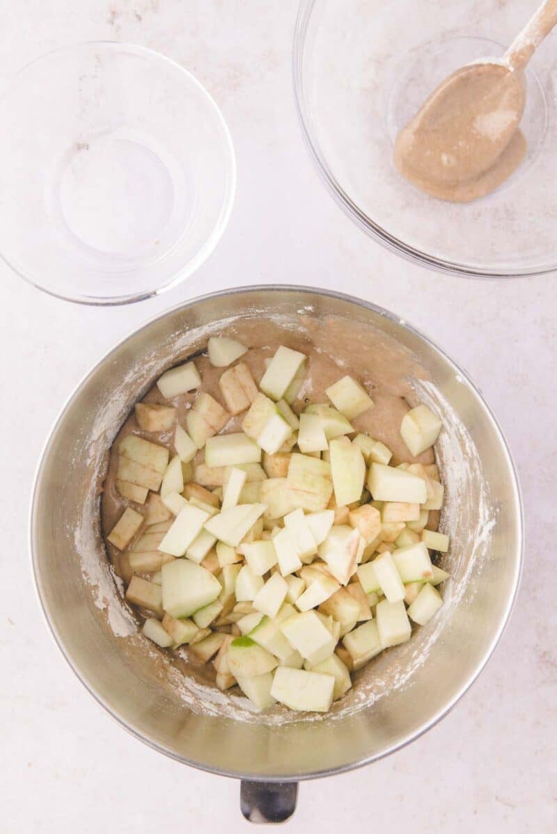 Chopped apples in a mixing bowl with cake batter, with a second bowl and a spoon nearby.