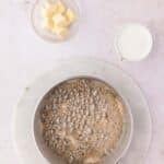 A saucepan of bubbling caramel on a marble board, with a small bowl of butter cubes and a small pitcher of cream nearby.