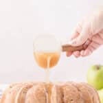 Hand pouring caramel glaze from a glass pitcher onto a bundt cake.