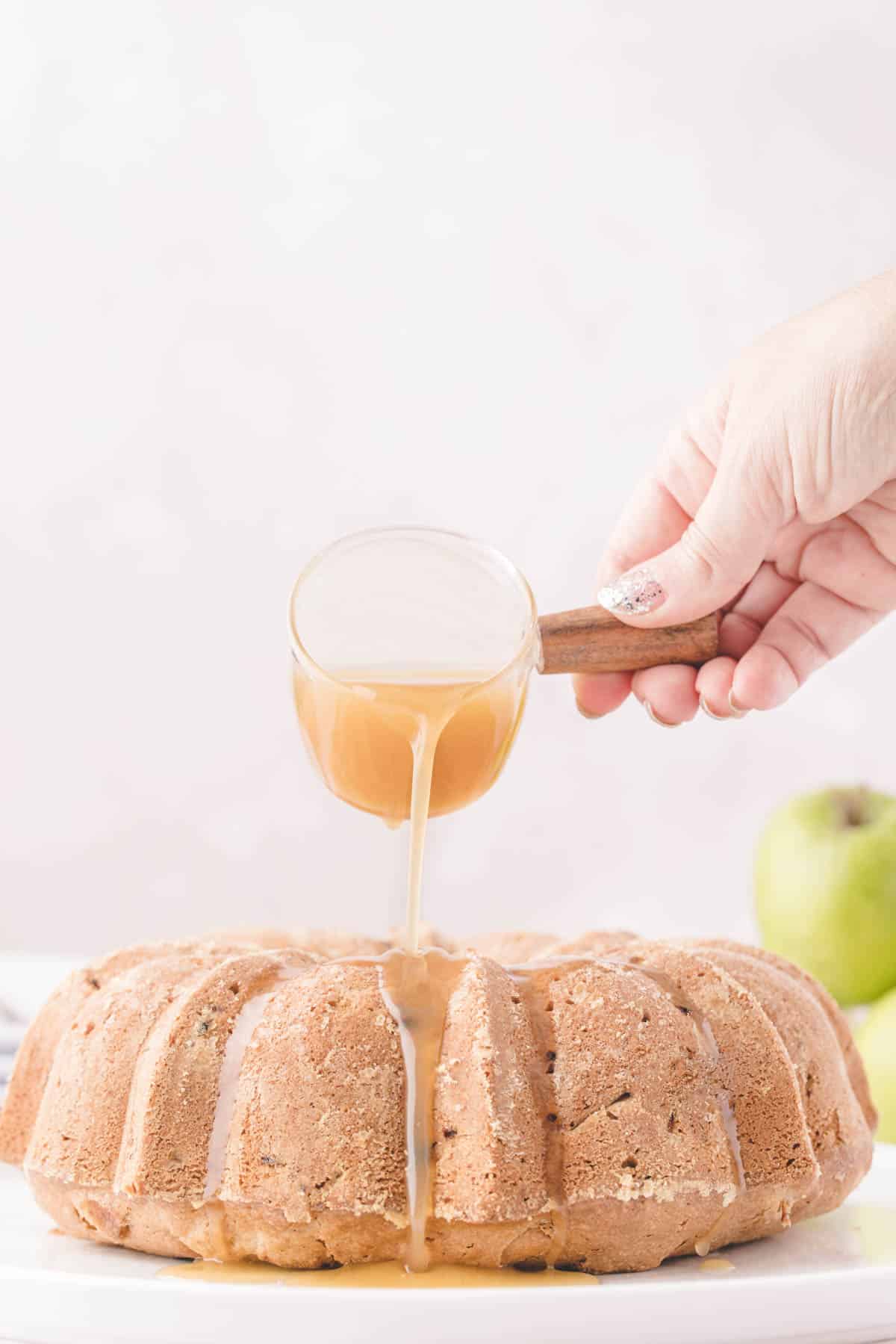 Hand pouring caramel glaze from a glass pitcher onto a bundt cake.