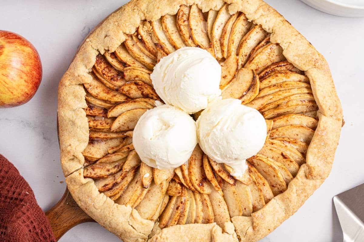 Apple galette topped with three scoops of vanilla ice cream, next to a fresh apple.