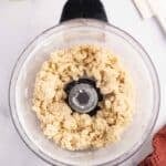 Crumbled pie dough inside a food processor bowl, with sliced apples and a spatula nearby.