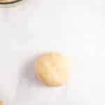 A ball of dough on parchment paper, with a bowl of sliced apples and a dish of melted butter nearby.