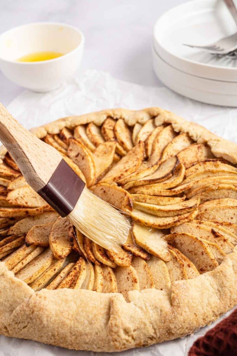 A pastry brush applies glaze to a raw apple galette.