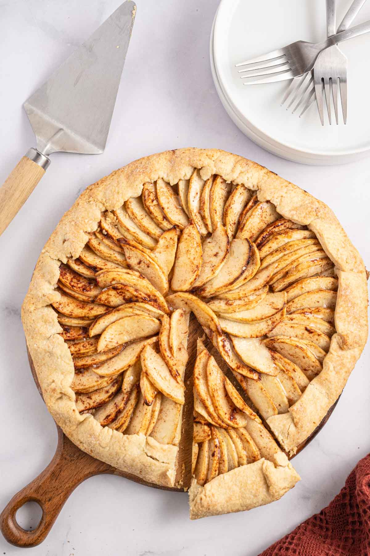 Apple galette on a wooden serving board with a cake server and two forks on plates nearby.