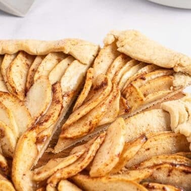 Rustic apple tart with sliced apples and a folded pastry crust on a wooden board.