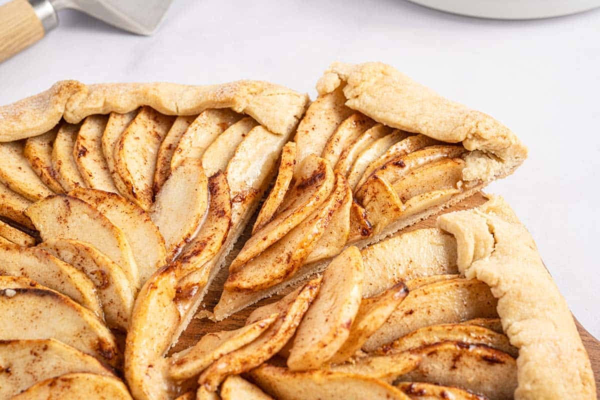 Rustic apple tart with sliced apples and a folded pastry crust on a wooden board.