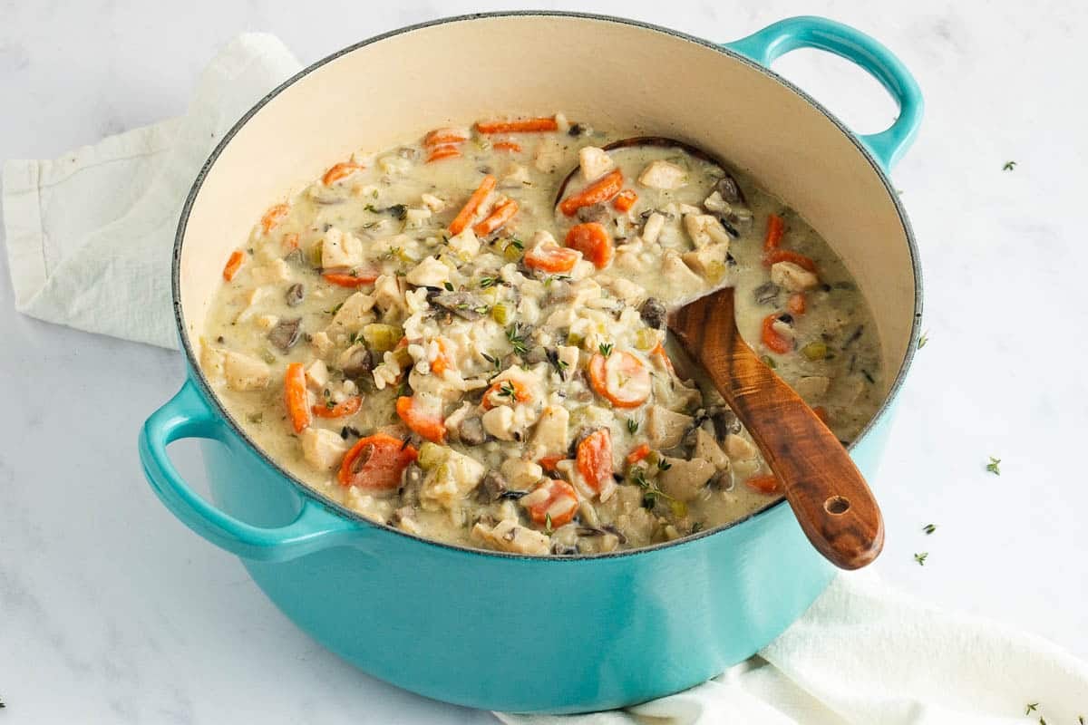 Creamy chicken and wild rice soup in a teal Dutch oven with a wooden spoon.