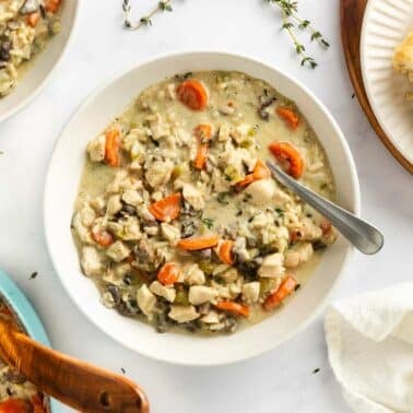 A bowl of chicken and wild rice soup with carrots and mushrooms, served with slices of crusty bread.
