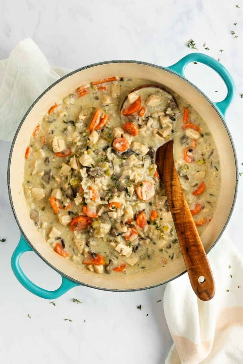A turquoise dutch oven filled with creamy chicken and wild rice soup, stirred with a wooden spoon.