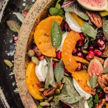 Harvest salad in a wooden bowl with roasted squash slices, fresh figs, pomegranate seeds, pecans, and greens.