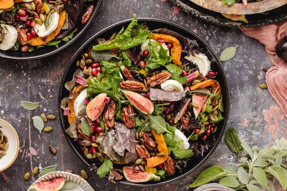 Salad with fresh figs, pecans, pomegranate seeds, roasted squash, and cheese in a black bowl.