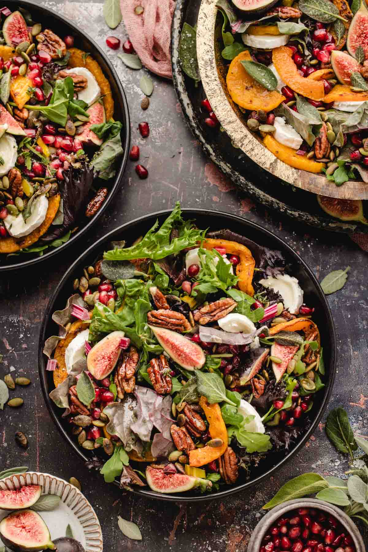 Three bowls of salad containing roasted squash, fresh figs, pecans, pomegranate seeds, and goat cheese.