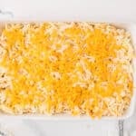A rectangular white baking dish filled with a mixture of shredded potatoes and topped with shredded cheddar cheese.