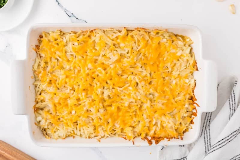 A rectangular baking dish filled with shredded hash brown casserole topped with melted cheddar cheese.