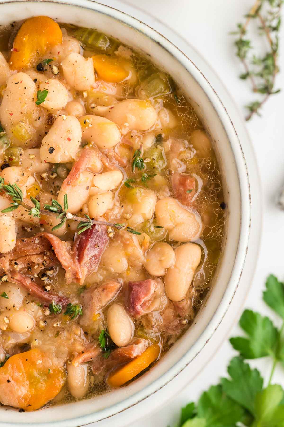 A bowl of navy bean and ham soup garnished with fresh thyme.