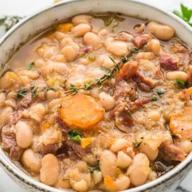 A bowl of white bean and ham soup with sliced carrots and fresh herbs.