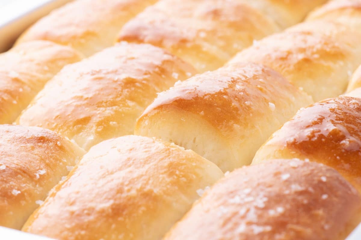 A pan of golden-brown dinner rolls topped with coarse salt.