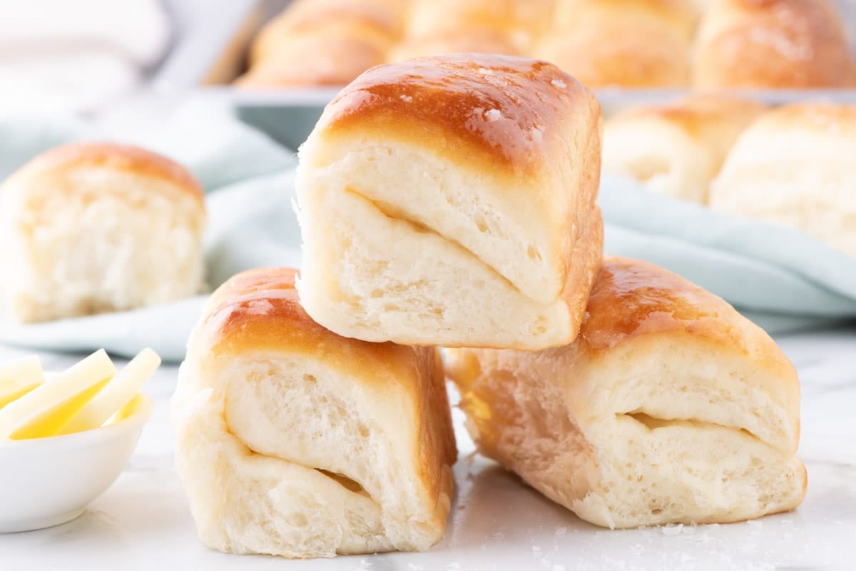 A stack of three golden-brown dinner rolls with a small bowl of butter.