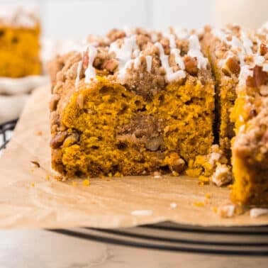 A slice cut from a pumpkin coffee cake topped with nuts and white icing on a wire cooling rack.