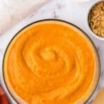 A glass bowl of orange purée, with small bowls of melted butter and crushed crackers nearby.