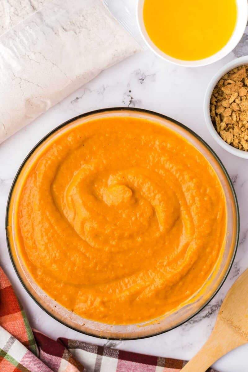 A glass bowl of orange purée, with small bowls of melted butter and crushed crackers nearby.