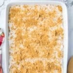 A rectangular baking dish filled with a pumpkin dump cake, alongside small bowls of melted butter and pecans.