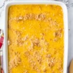 A rectangular baking dish filled with a golden butter and crumb mixture, accompanied by small bowls of caramel sauce and pecans.
