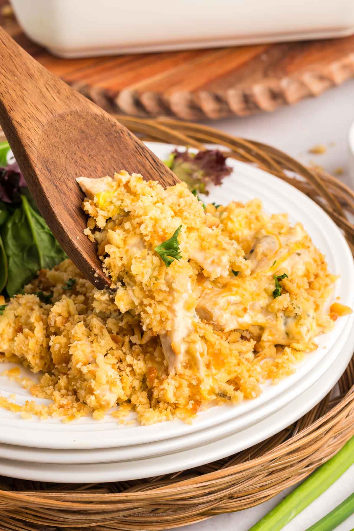 A wooden spoon lifting a serving of cheesy ritz cracker chicken casserole topped with breadcrumbs from a plate.