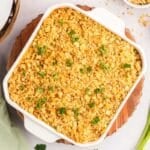 A square white baking dish filled with a ritz cracker chicken casserole topped with golden breadcrumbs and garnished with parsley, served on a wooden board with an onion and green onions.
